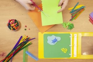 photo shows a pair of hands cutting green paper over a table containing parts from the Tactile and CVI Book Builder kits