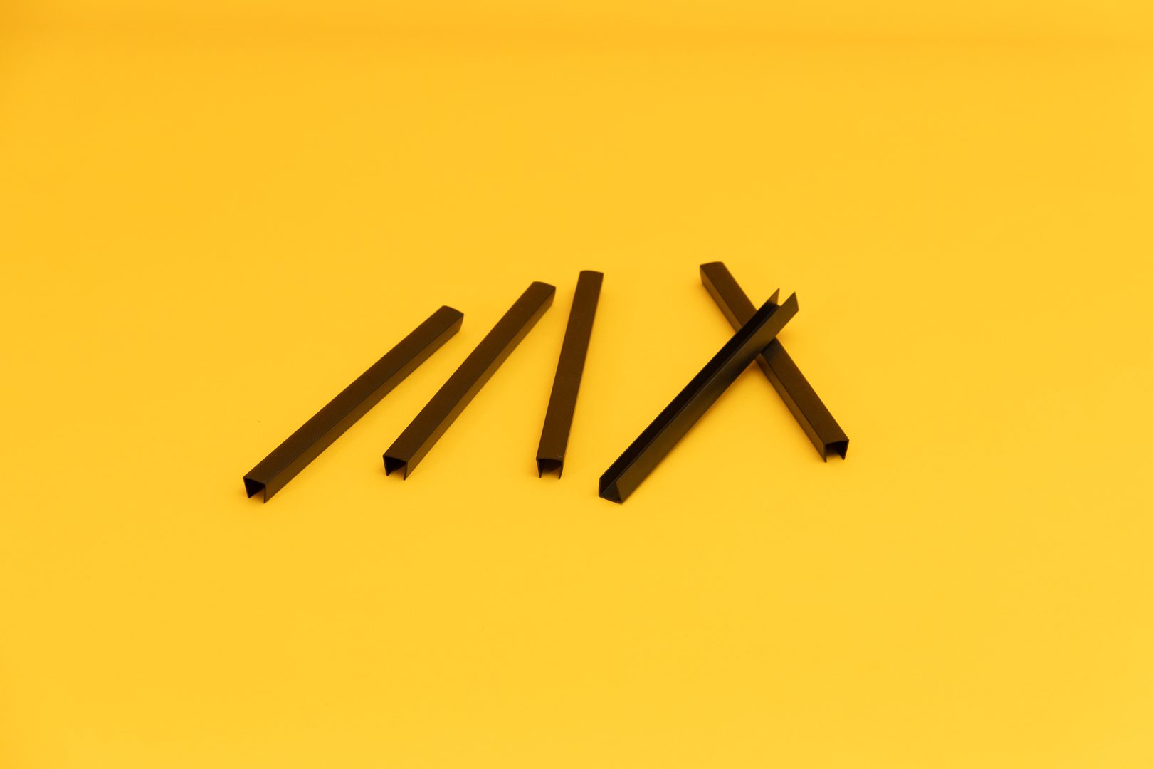 : A close up of six black U-Channels laid out on a yellow background.