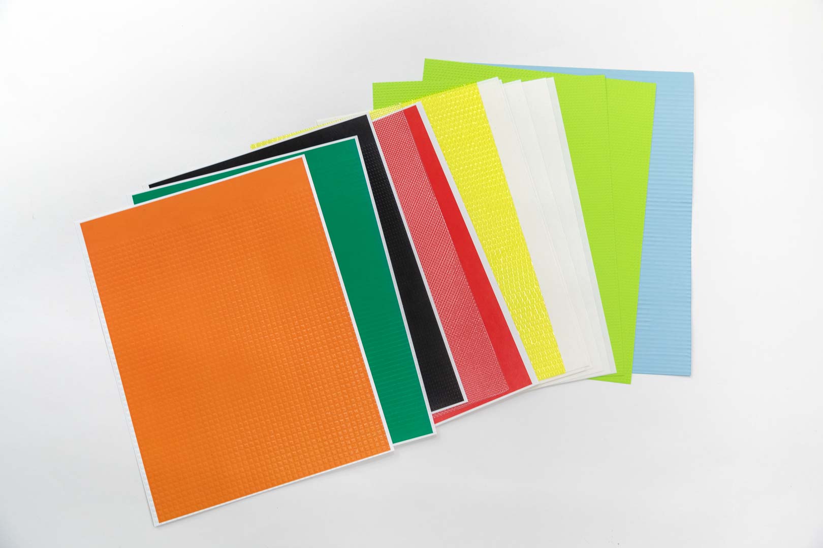 A stack of multi-colored textured paper spread across on a white surface.